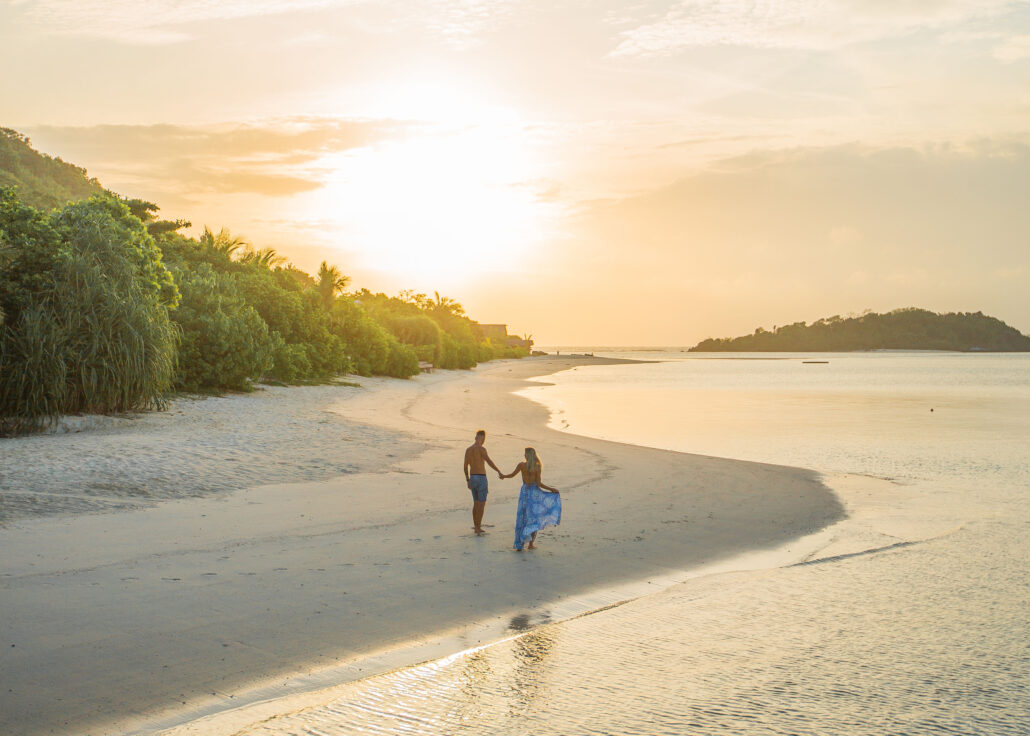 white young couple holding hands walking in sunrise beach muerba view